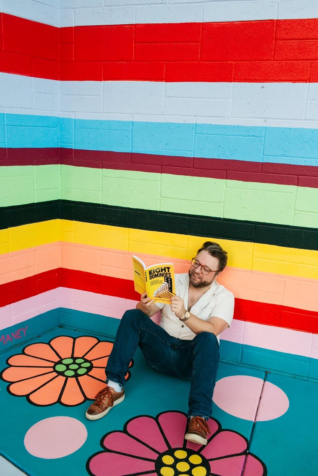 Jake Tlapek reading Eight Dominoes in a corner painted with rainbow stripes